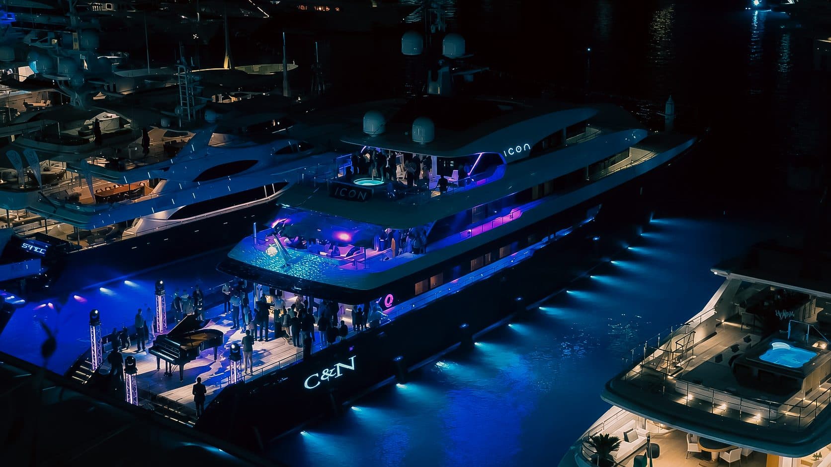 Yacht illuminé de bleu à quai, un piano à queue installé sur le ponton