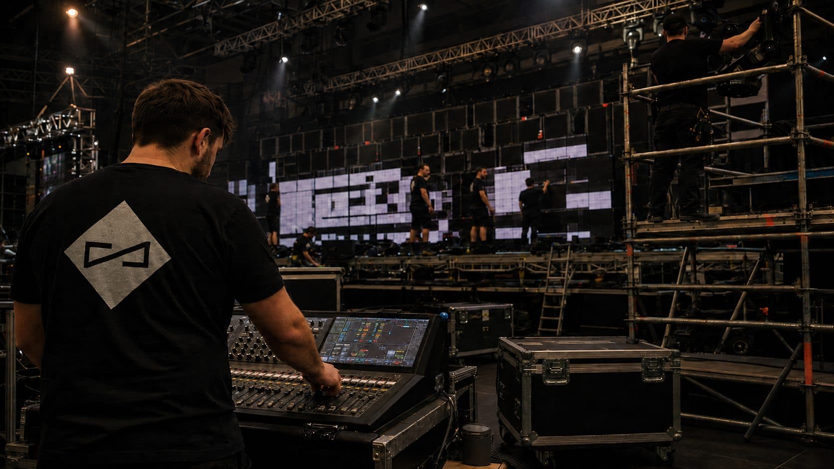 Technicien à la console de mixage devant un mur d’écrans LED en cours de calage, structures et flight cases autour