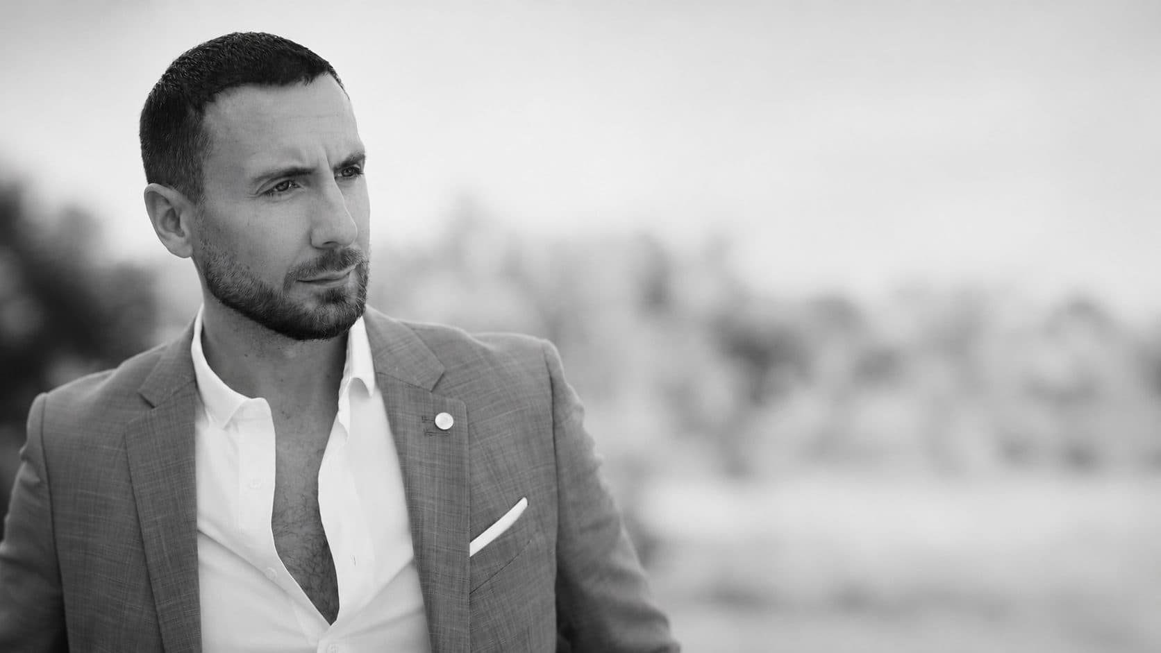 Portrait en noir et blanc de Julian Marshall, en costume clair et chemise ouverte, le regard porté au loin