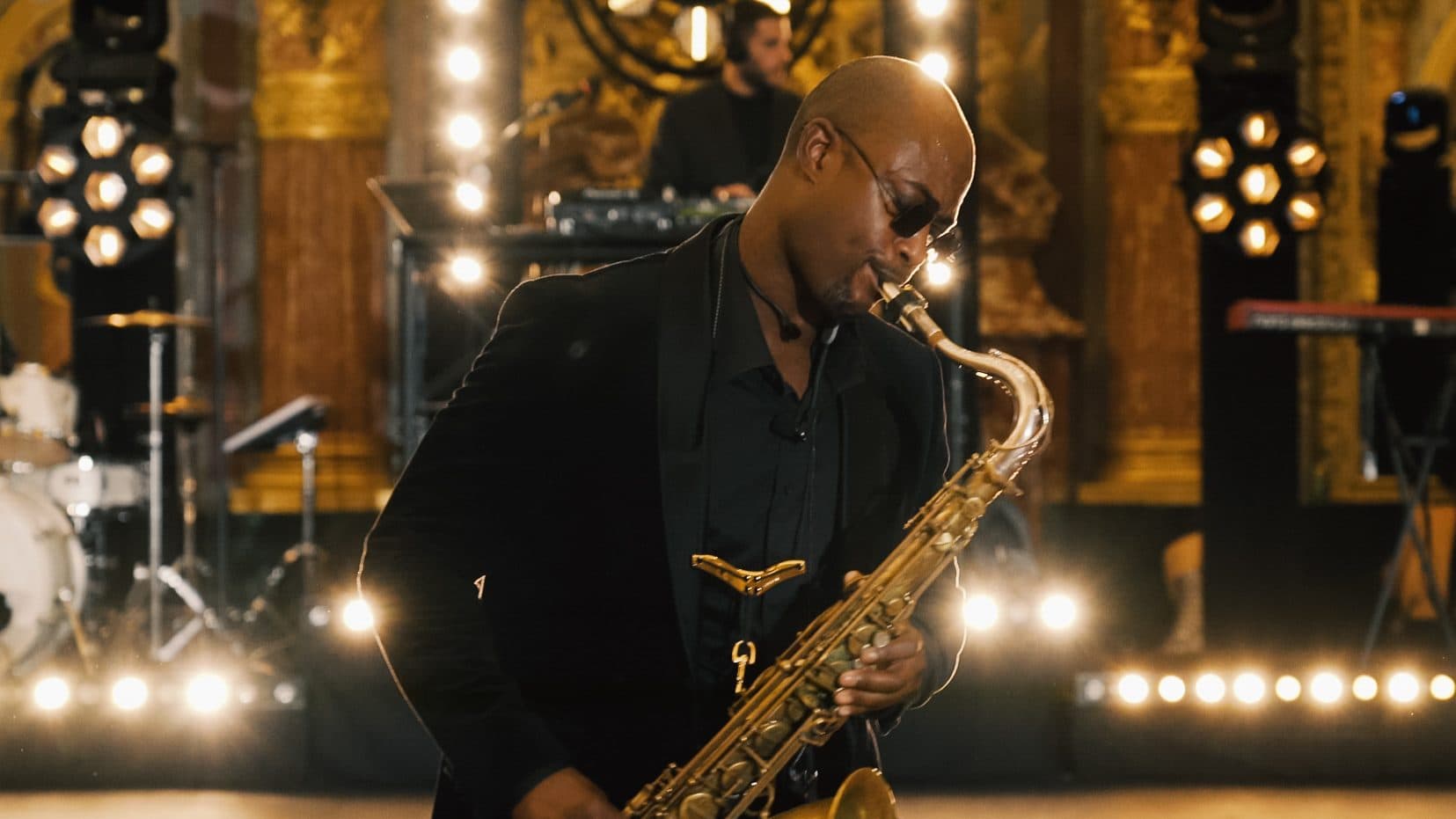 Saxophoniste en costume noir jouant dans une salle dorée aux lustres allumés
