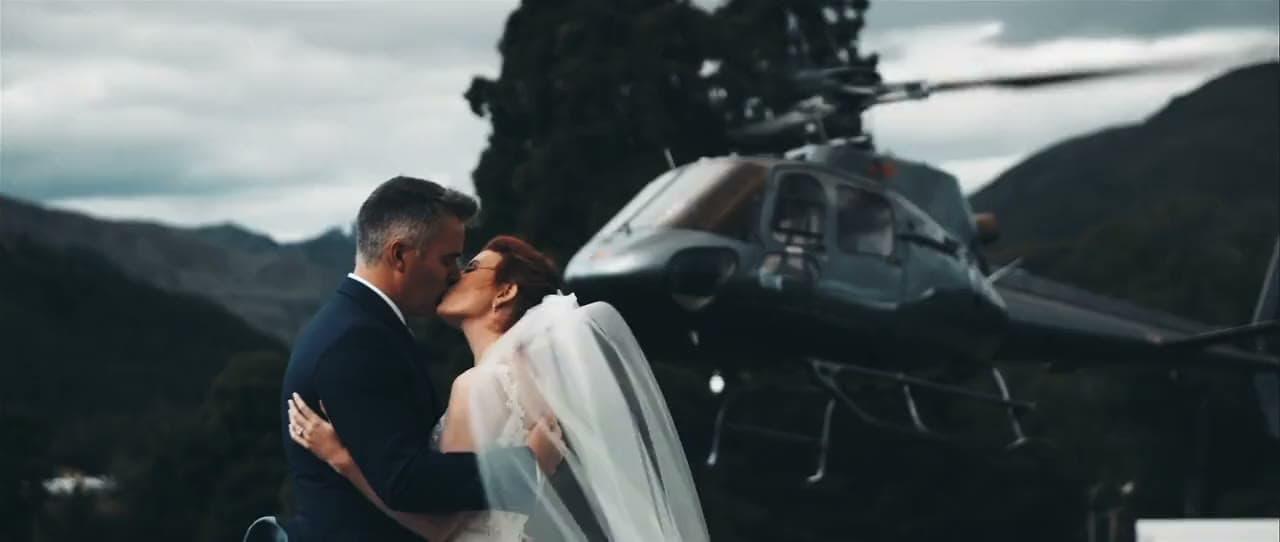 Mariés s’embrassant devant un hélicoptère posé en montagne, la mariée en robe blanche et voile